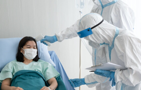2 healthcare staff checking the patients' temperature in medical masks and protective gowns