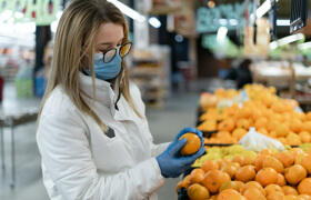 a female wearing a green surgical mask is selecting oranges in front of the fruit shop